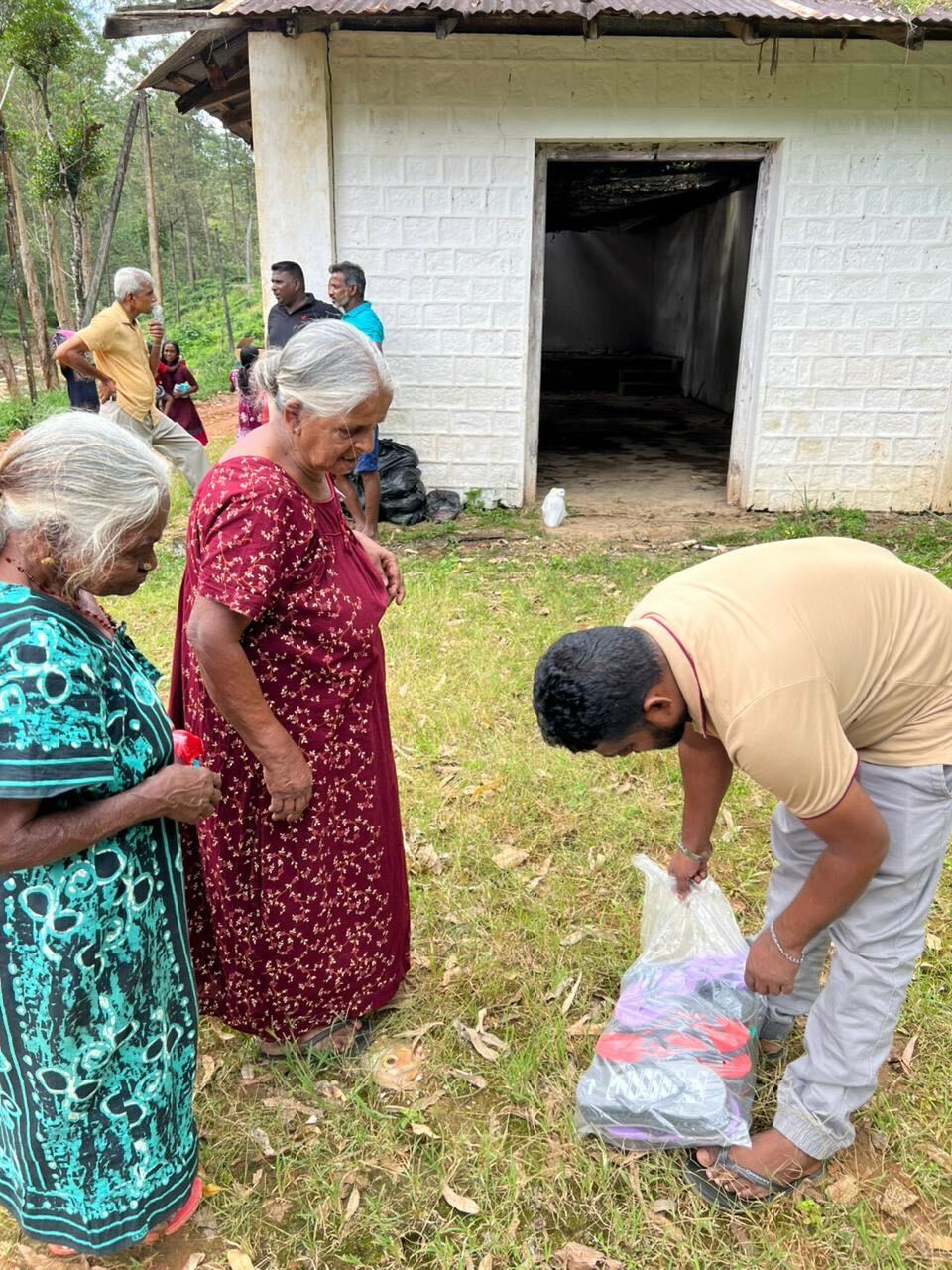 A man hands relief supplies to two women in a rural Sri Lankan jungle village.