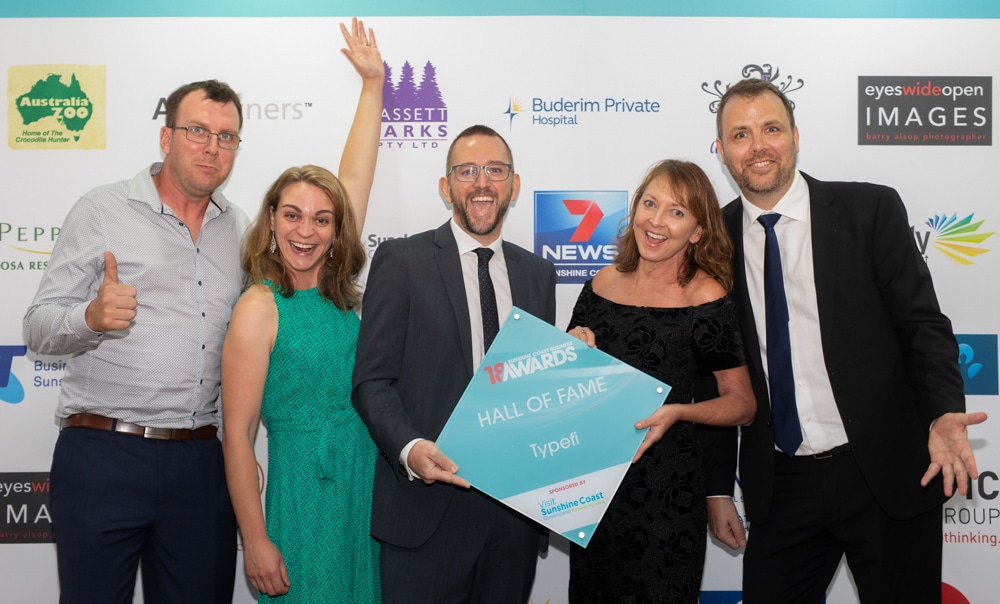 The Typefi team holding up their 2018 Hall of Fame trophy in front of a Sunshine Coast Business Awards backdrop.
