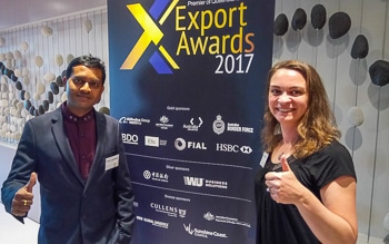 Typefi Senior Engineer Dinesh Amarasekara and Marketing Associate Shanna Bignell give the thumbs-up in front of a 2017 Premier of Queensland's Export Awards banner.