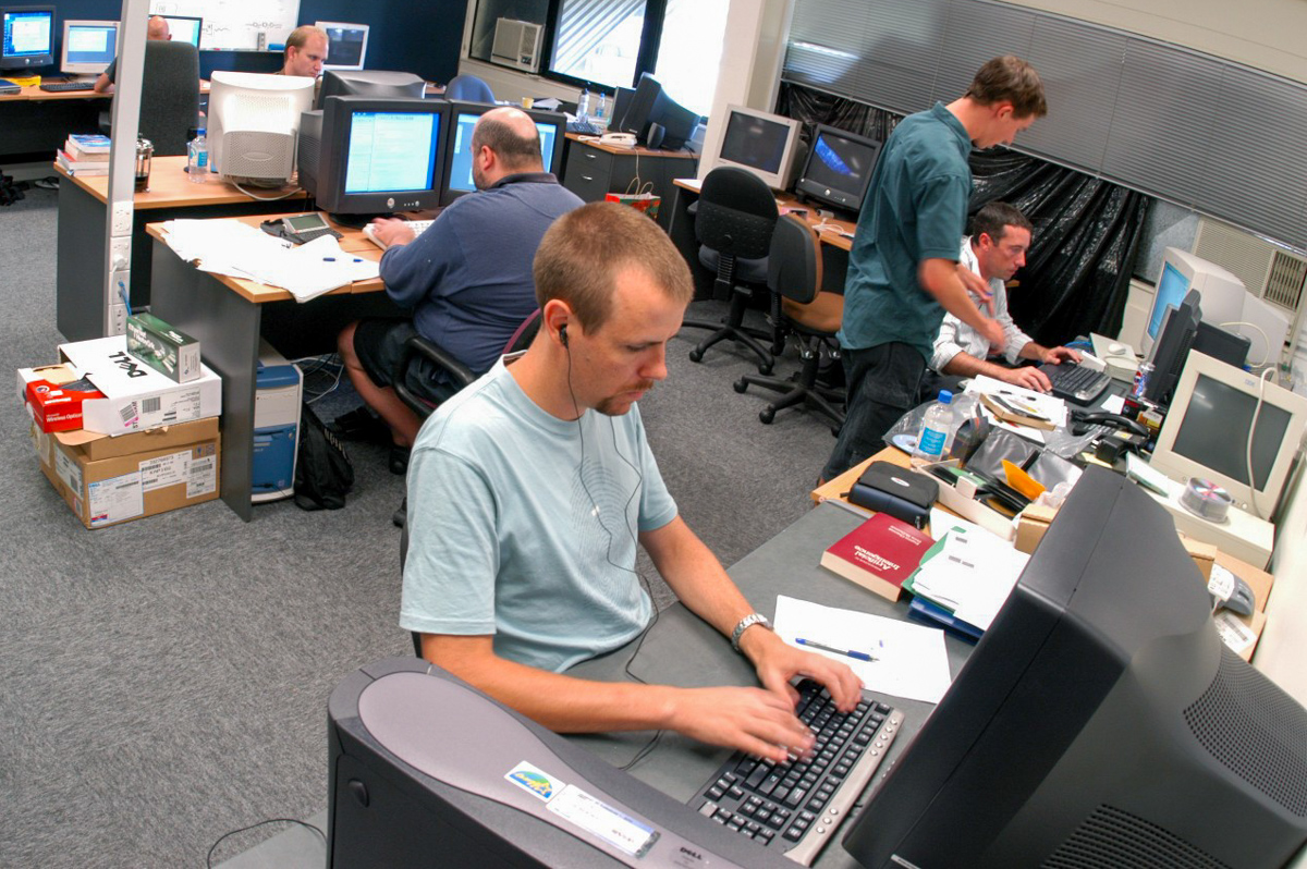 A group of software engineers at work in an office with Ben Hauser working at his computer in the foreground. The technology looks very dated. All the computers have separate CPU boxes and large free-standing monitors.