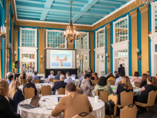 Kara Laufer-Levesque presents to a large audience at the 2019 Typefi User Conference. On the screen is an image of balanced rocks by the ocean.