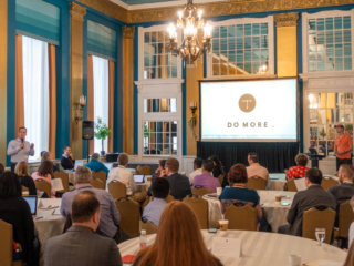 Guy van der Kolk and Caleb Clauset presenting to a large audience at the 2019 Typefi User Conference. The screen shows the Typefi logo and tagline DO MORE.
