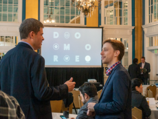 Per Thrane-Nielsen chats with Tim Siers during morning tea. A screen in the background displays the Typefi tagline DO MORE.
