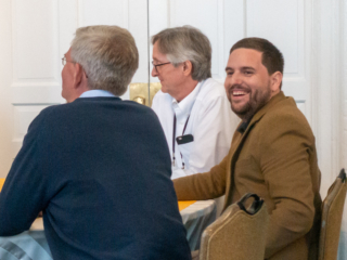Candid photo of Damian Gibbs, John Muenning and Jaume Balmes seated at a table. Jaume is laughing.