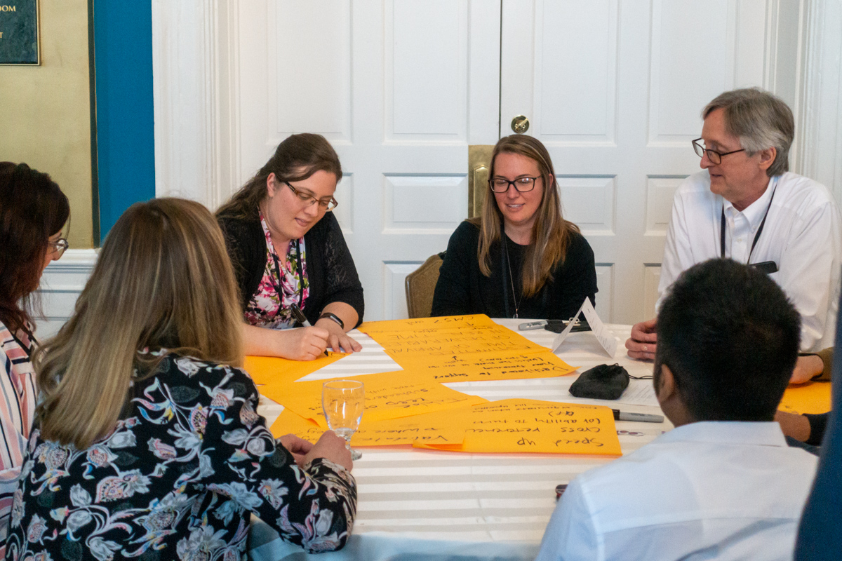 A group of guests writes product ideas on large yellow post-it notes.