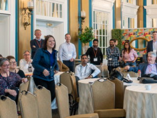 Alyssa Brunner getting up from the audience to do her presentation, while the audience smiles supportively.