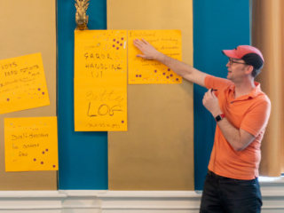 Caleb Clauset gestures to the assembled feedback post-it notes. The notes say 'Tables keep options', 'Dual-direction live content flow', 'Error handling', 'Better log messages', 'Dashboard'.