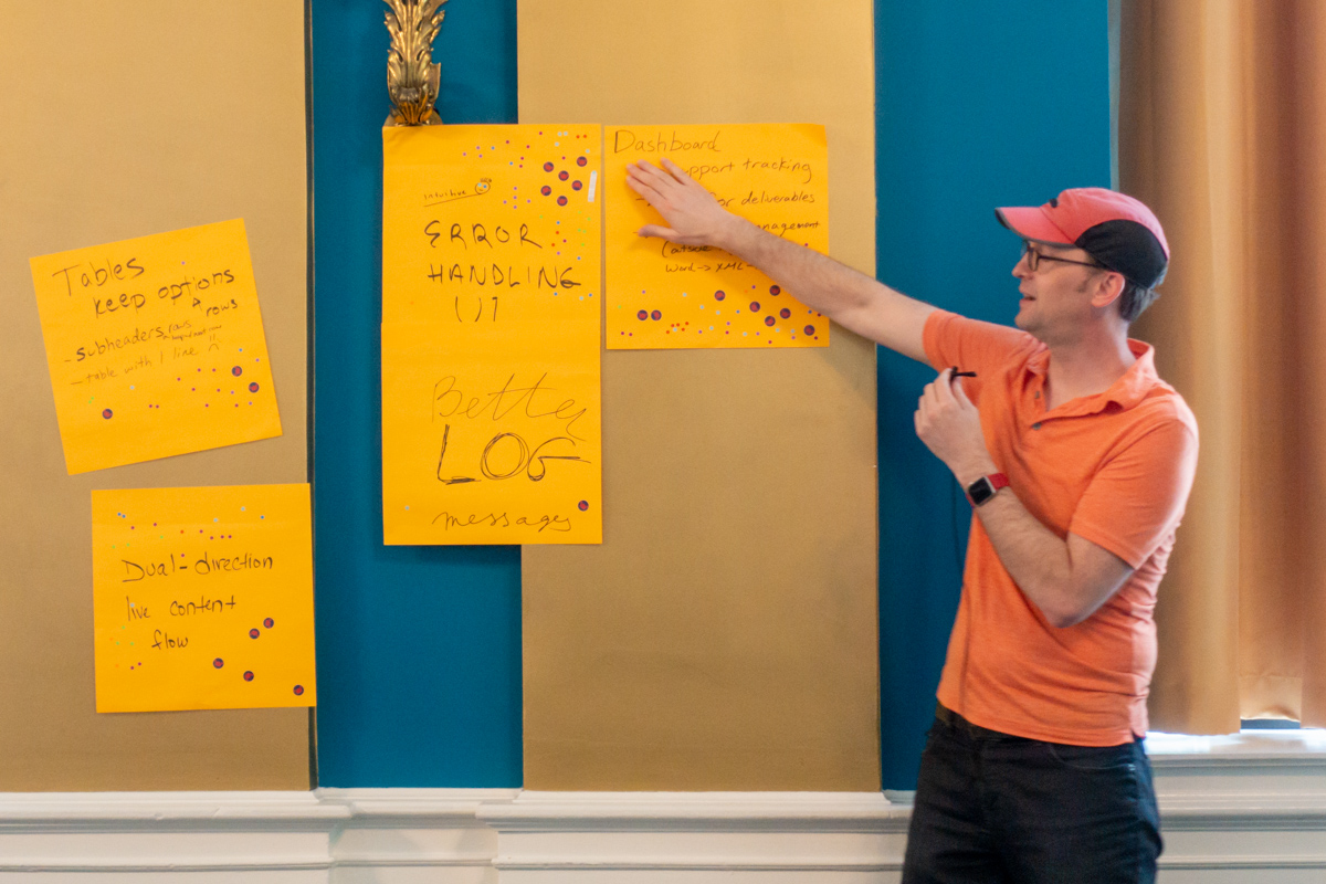 Caleb Clauset gestures to the assembled feedback post-it notes. The notes say 'Tables keep options', 'Dual-direction live content flow', 'Error handling', 'Better log messages', 'Dashboard'.
