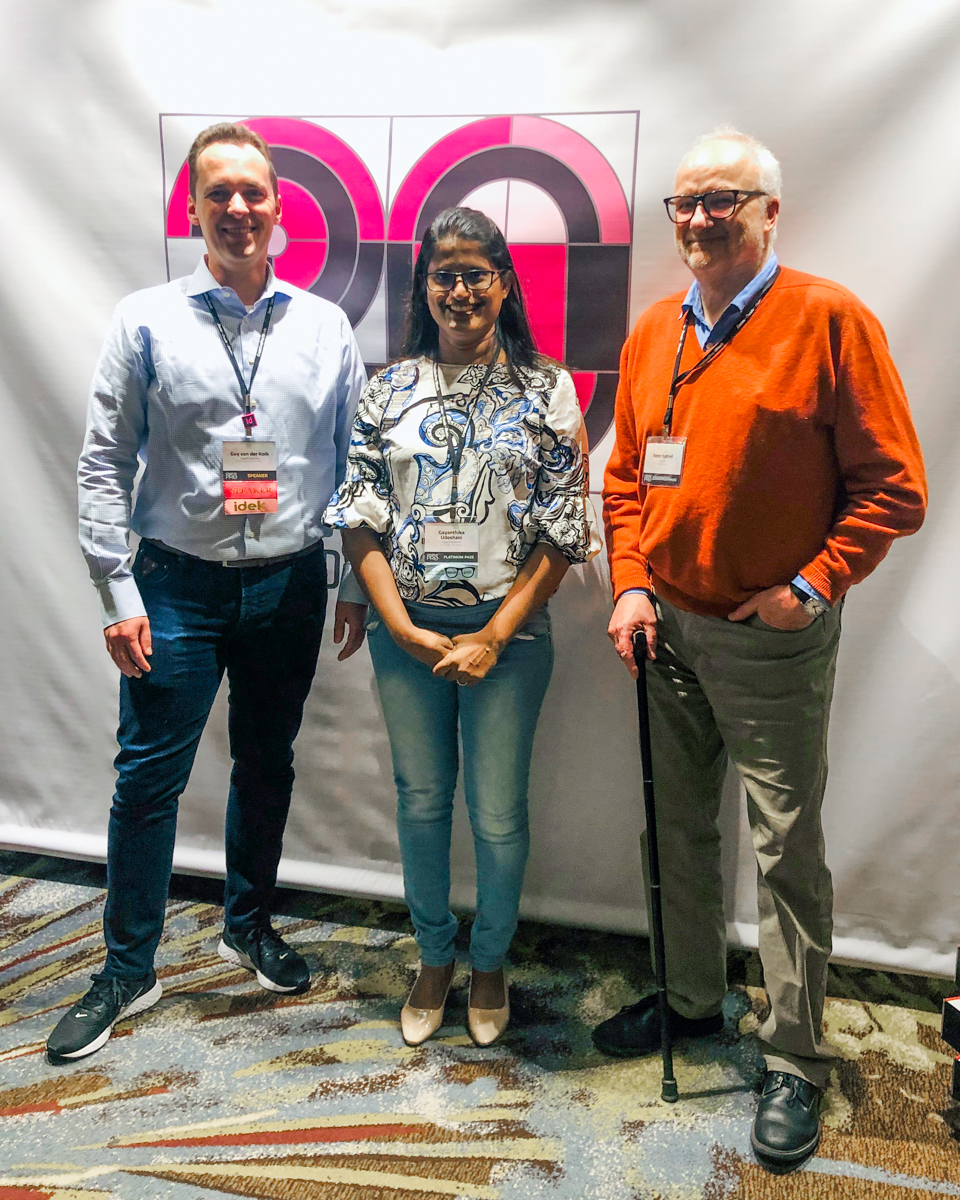 Guy van der Kolk, Gayanthika Udeshani and Peter Kahrel stand in front of a large banner displaying Adobe's official '20 years of InDesign' artwork.