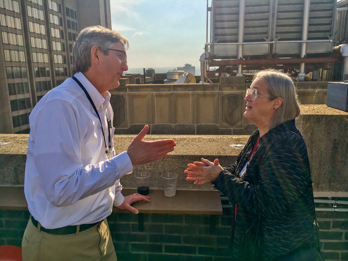John Muenning and Debbie Lapeyre deep in conversation at the rooftop bar, with a bunch of other Baltimore rooftops and buldings visible in the background.