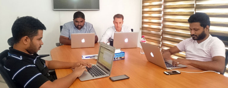 Typefi Professional Services team members Dinitha, Dilshan, Eric, and Dilum, seated around a desk working on laptop computers as part of a Typefi training session.