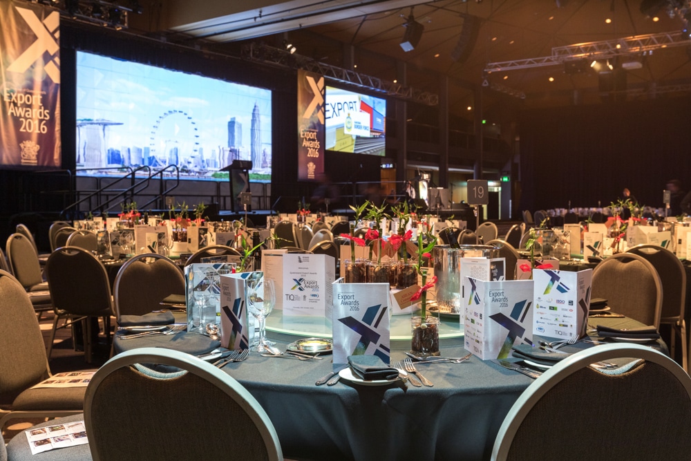 The Plaza Ballroom at the Brisbane Convention and Exhibition Centre set up for the Premier of Queensland's Export Awards. Guests have not yet arrived but the tables are set and there is an image of the Brisbane Wheel and skyline displayed on a large screen over the stage.