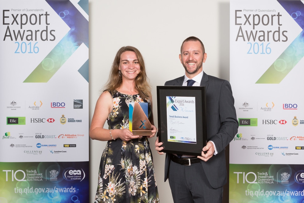 Typefi Marketing Associate Shanna Bignell and Financial Controller Michael Cousins display the 2016 Premier of Queensland’s Small Business Export Award in front of two large Export Awards banners.