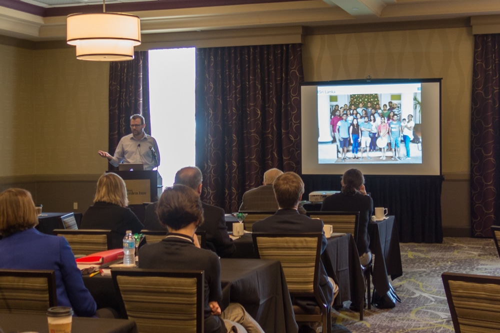 Typefi VP Engineering Ben Hauser speaks to the audience at the 2017 Typefi User Conference. The screen behind him displays a group photo of Typefi's Sri Lankan team at its 2016 end-of-year gathering.