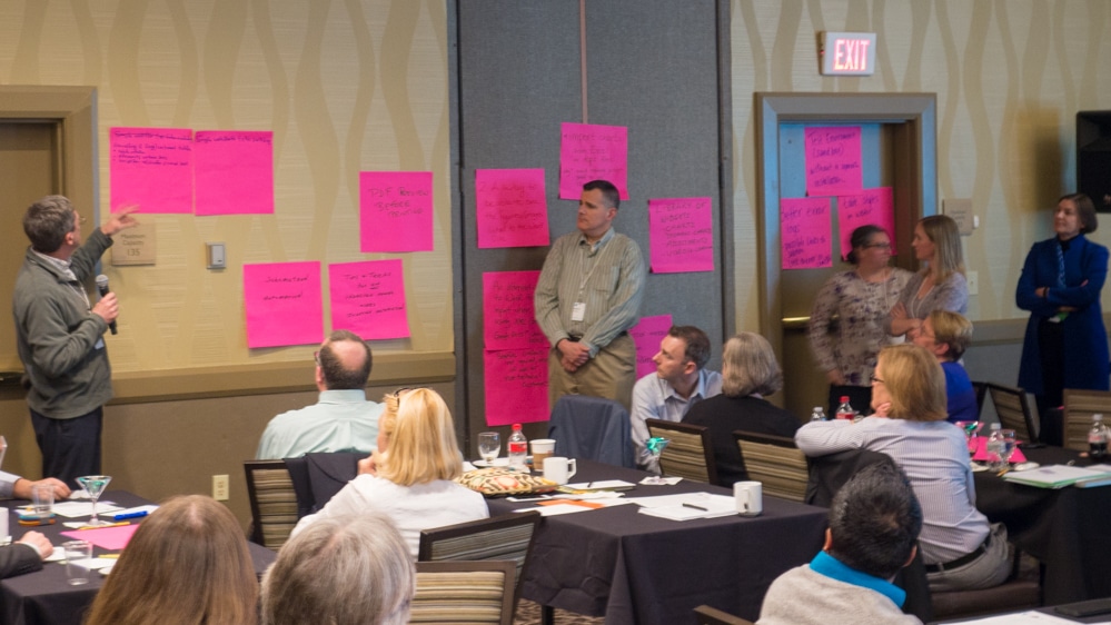 Allan Heathman from Sheridan Journal Services and Patrick Gibbons from IEEE present to audience members at the 2017 Typefi User Conference. A display of large pink post-it notes stuck to the wall contain handwritten product feature requests.