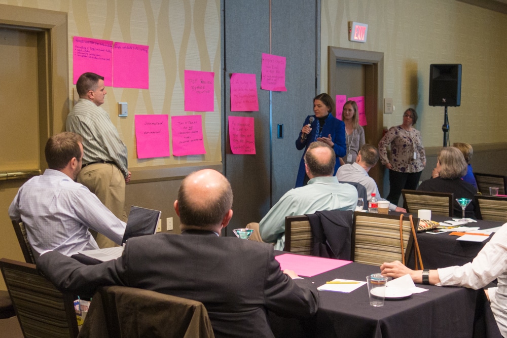 Linda Griffin Kean from the IMF presents to audience members at the 2017 Typefi User Conference. A display of large pink post-it notes stuck to the wall contain handwritten product feature requests.