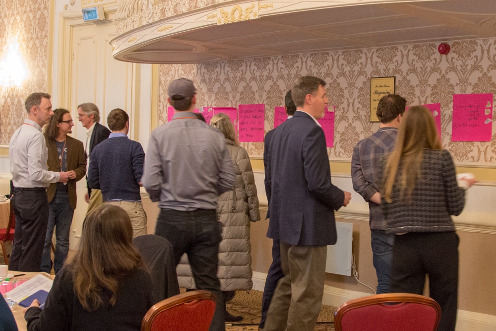 A group of attendees using stickers to vote on the product suggestions, which are written on large pink post-it notes stuck to the wall.