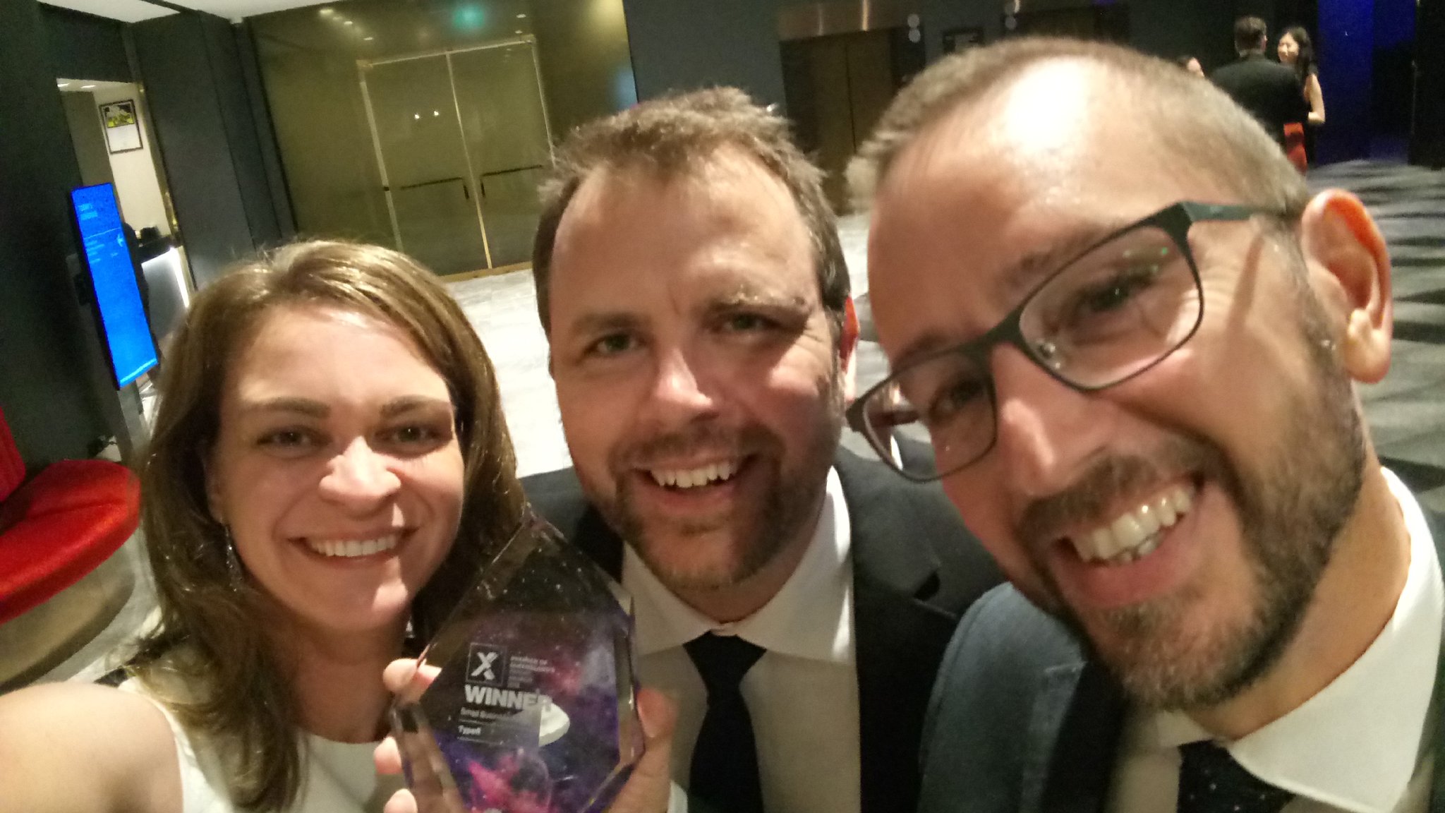 Shanna Bignell, Ben Hauser and Michael Cousins holding up Typefi's 2018 Premier of Queensland's Export Awards trophy, an engraved glass shard.