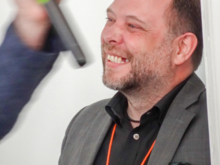 Stephen Laverick laughing as Karl Jankowski waves a microphone.